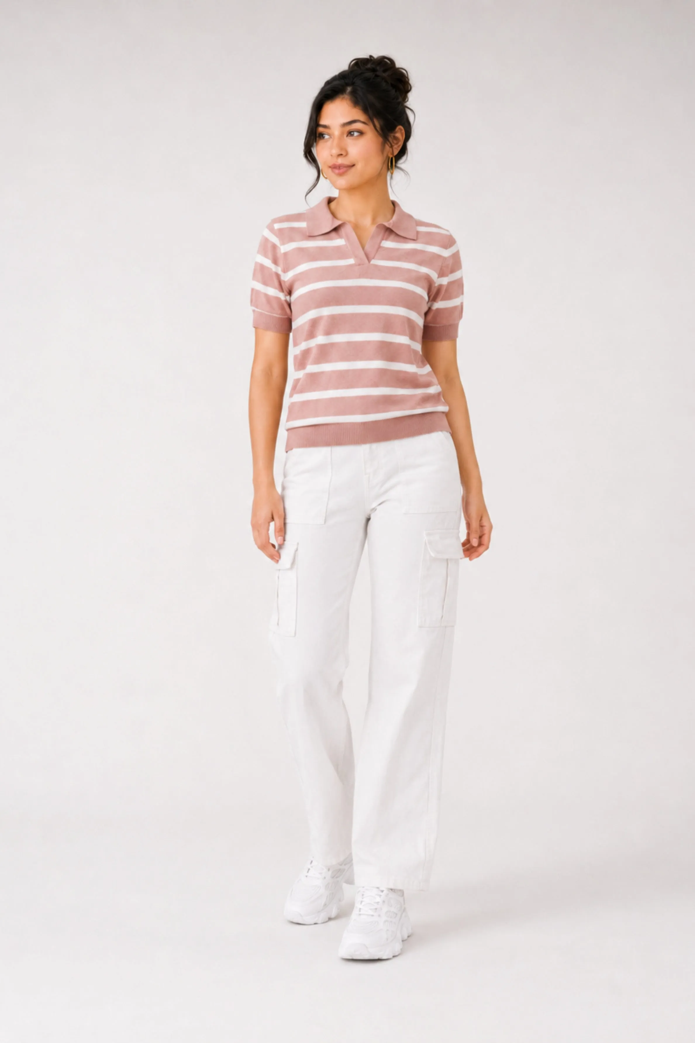 A model in a pink and white striped polo shirt with short sleeves and white cargo pants with pockets. White sneakers complete the look, set against a plain background.