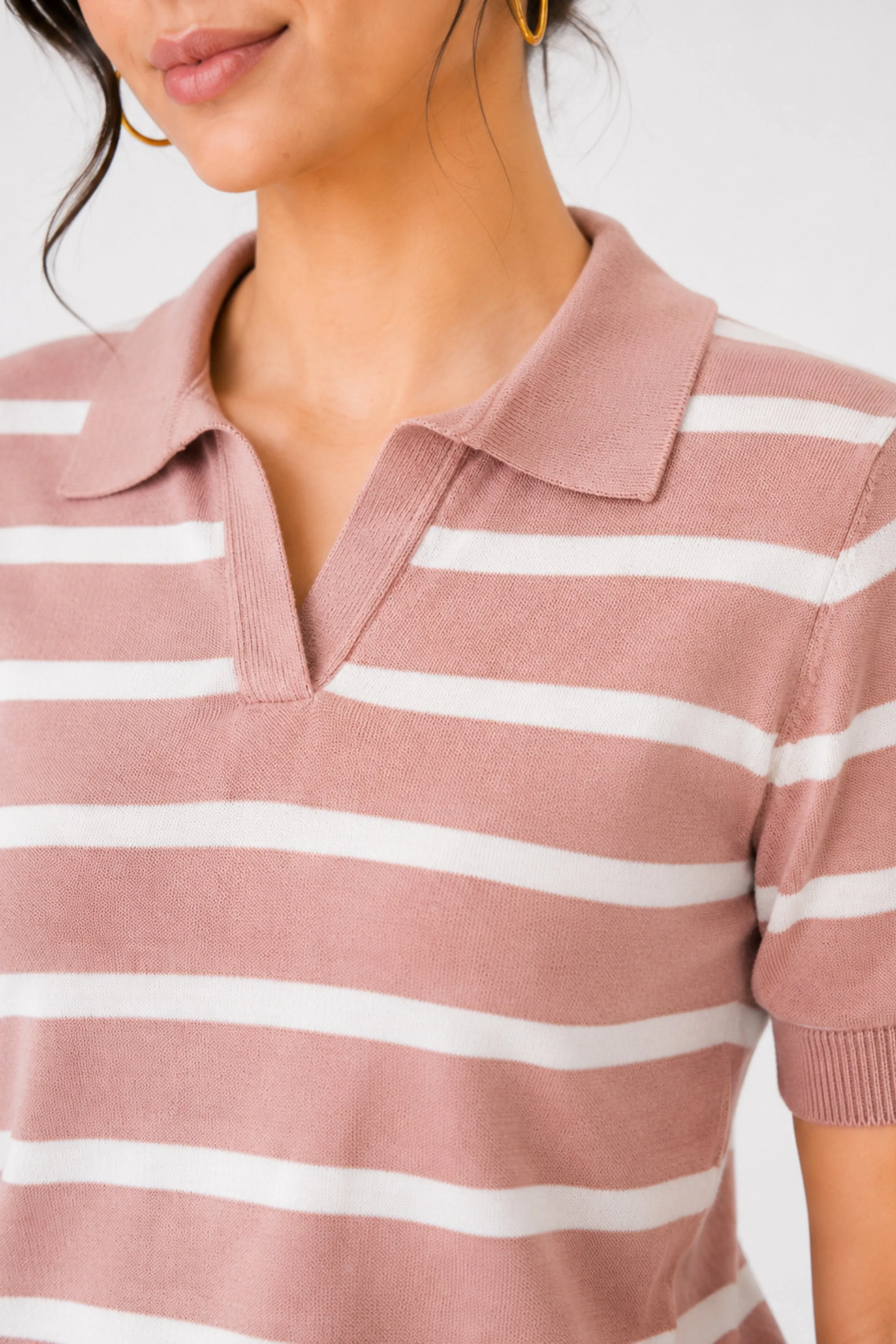 Close-up of pink and white striped knit polo shirt with a collar and short sleeves, worn by a model. Set against a simple neutral backdrop.