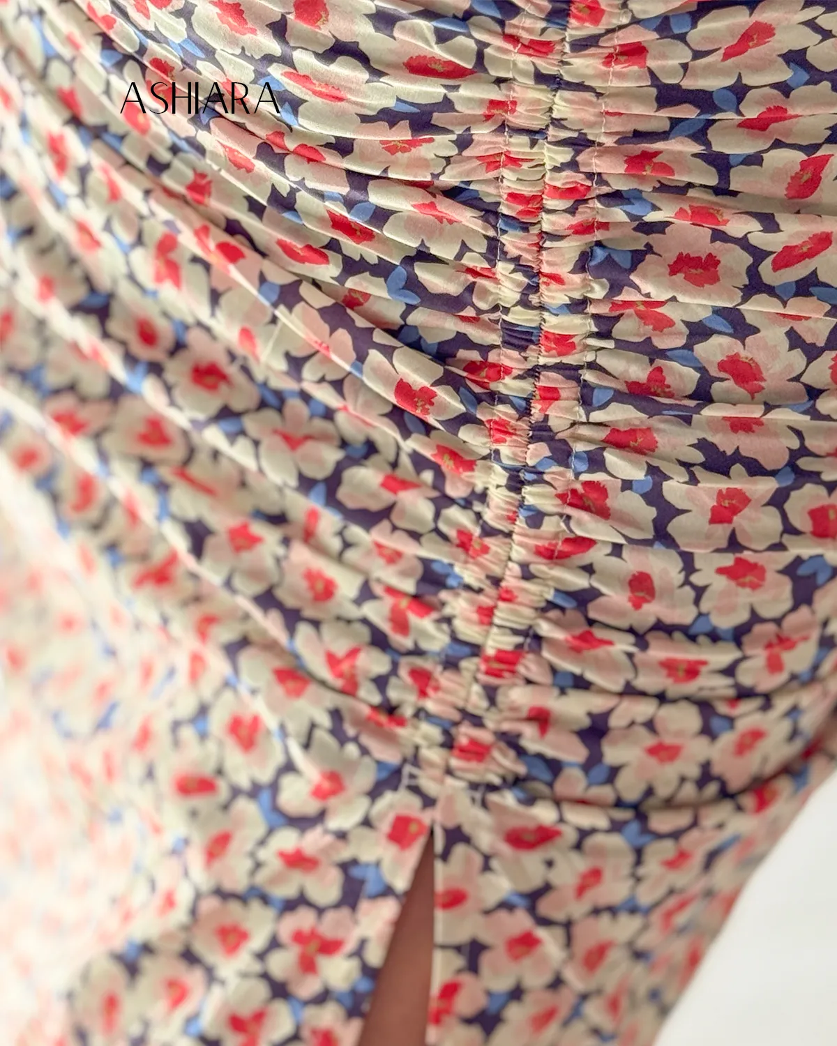 Close-up of a floral patterned skirt with a detailed ruching design and a high slit. The fabric displays small red and blue flowers. The brand 'ASHARA' is visible in the top left corner.